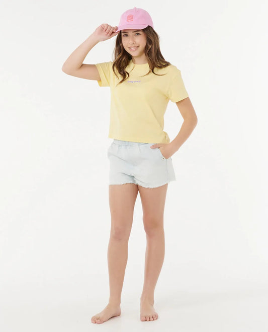Young girl wearing a yellow t-shirt, white shorts, and a pink cap on a white background