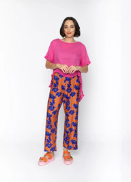Woman wearing a pink top and orange floral pants on a white background