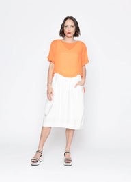 Woman wearing an orange top and white skirt on a white background