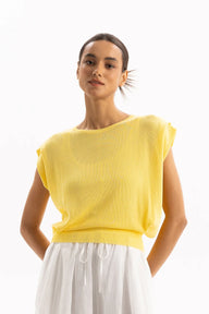 A woman wearing a bright yellow knit top with wide cap sleeves and a relaxed fit, paired with white drawstring trousers, photographed against a clean white studio background.