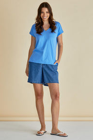 Woman wearing a blue t-shirt and denim shorts against a beige background