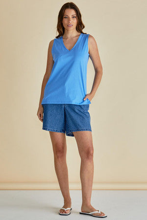Woman wearing a blue sleeveless top and denim shorts against a beige background