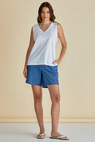 Woman wearing a white sleeveless top and blue shorts against a beige background