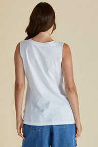 Woman wearing a white sleeveless top and blue pants on a beige background
