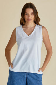 Woman wearing a white sleeveless top and blue jeans on a beige background