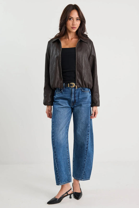 Woman wearing a dark leather jacket, black top, and blue jeans on a white background