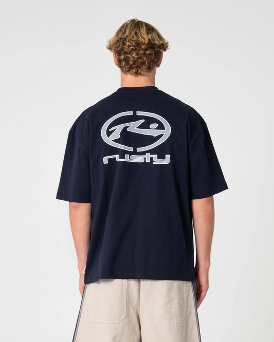 A man viewed from behind wearing a navy blue short-sleeve t-shirt with a large white and silver graphic logo on the back, paired with beige shorts, against a light gray studio background.