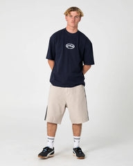 Person wearing a navy blue t-shirt with a logo and beige shorts on a white background
