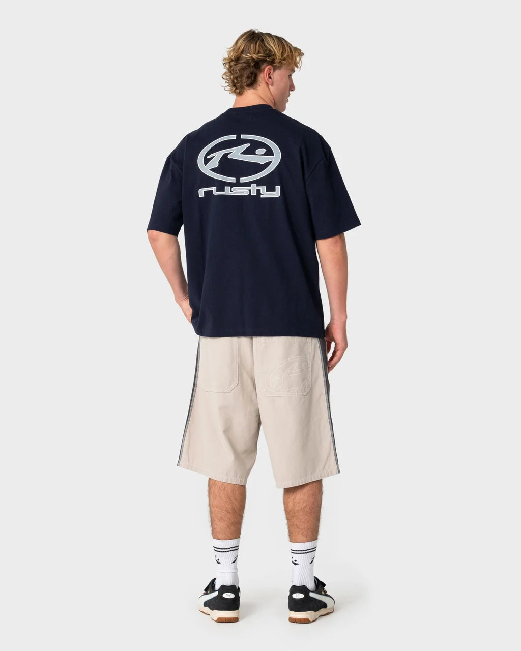 Person wearing a navy blue t-shirt with a logo on the back, standing against a white background