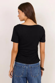 A woman shown from the back wearing a black short-sleeve boat-neck t-shirt and blue jeans, standing against a plain off-white background.