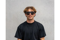 Person wearing black sunglasses and a black t-shirt against a gray background