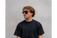 Person wearing sunglasses and a black t-shirt against a gray background