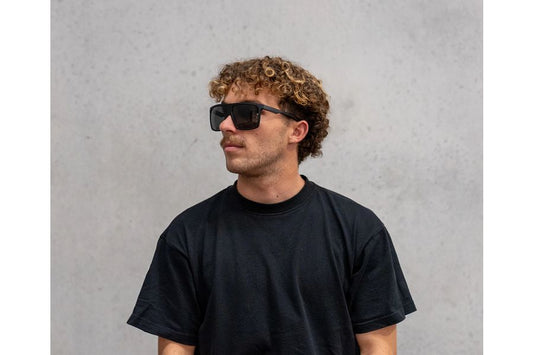 Person wearing sunglasses and a black t-shirt against a gray background