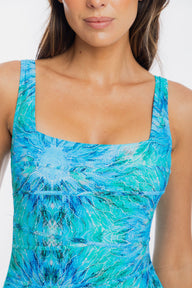 A close-up of a woman wearing a sleeveless top with a square neckline and a blue and turquoise abstract marbled pattern.