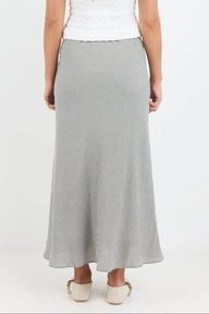 A woman wearing a light gray textured maxi skirt with a white top and beige shoes, shown from the back against a plain white studio background.