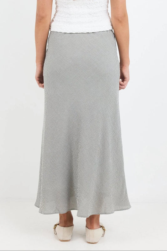 A woman wearing a light gray textured maxi skirt with a white top and beige shoes, shown from the back against a plain white studio background.