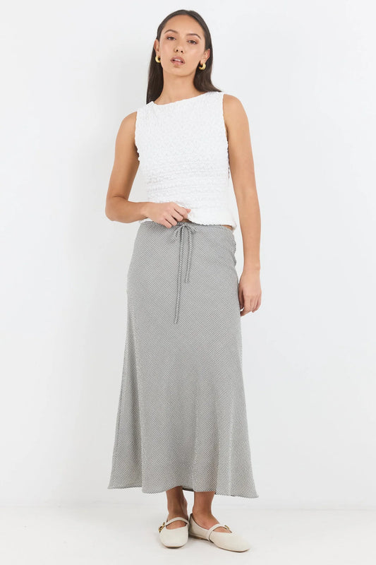 A woman modeling a white sleeveless textured top and a light gray midi skirt with a drawstring waist, paired with beige flats, against a plain white studio background.