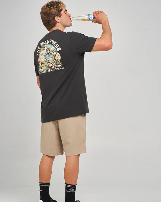 A man wearing a black graphic t-shirt and beige shorts, shown from the back as he drinks from a bottle. The t-shirt features a large graphic print with the text 'THE ROAD KEEPER' and 'STRAIGHT ENROLLED'.