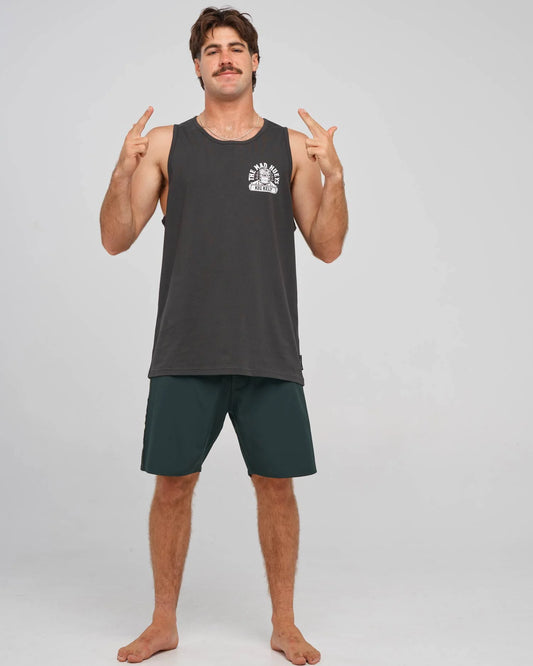 A man modeling a dark gray sleeveless tank top with a white chest graphic and dark green athletic shorts, posing against a light gray studio background.