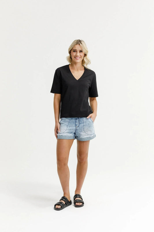 A woman modeling a black short-sleeve V-neck t-shirt, light-wash denim shorts, and black slide sandals against a plain white studio background.