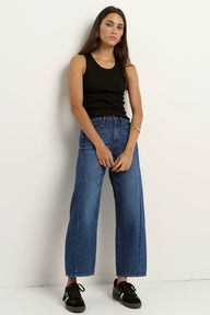 Woman wearing a black tank top and blue jeans against a white background