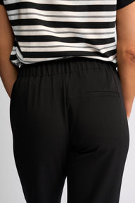 Close-up back view of a person wearing black elastic-waist pants with a side pocket and a black-and-white striped top.