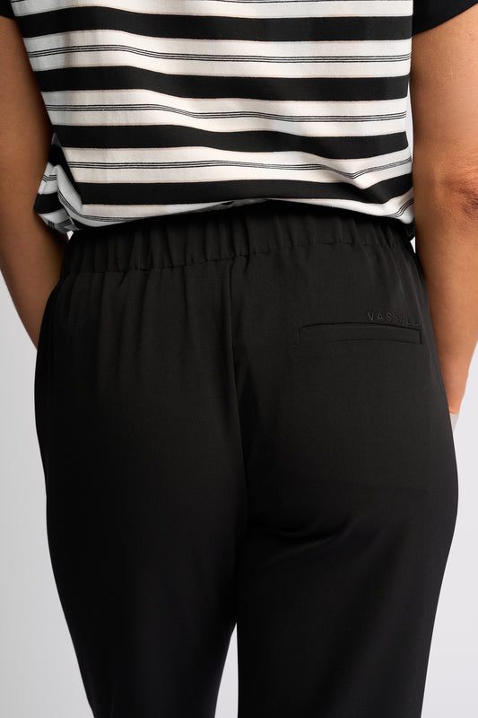 Close-up back view of a person wearing black elastic-waist pants with a side pocket and a black-and-white striped top.