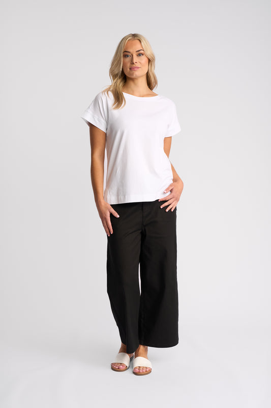 A woman modeling a white short-sleeve crewneck t-shirt and black wide-leg pants against a light gray studio background.