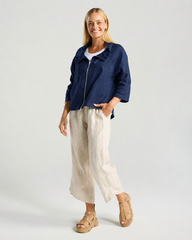 A woman modeling a navy zip-up jacket over a white top, paired with light beige linen wide-leg pants and tan platform sandals, against a light gray studio background.