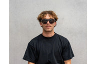 Person wearing sunglasses and a black t-shirt against a gray background