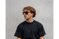 Man wearing sunglasses and a black t-shirt against a gray background