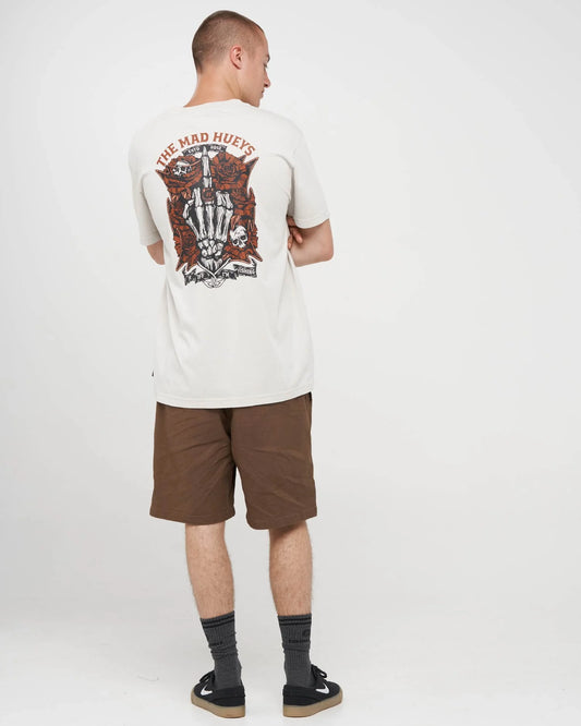 A man shown from the back wearing a cream-colored t-shirt with a large red and black graphic print on the back, paired with brown shorts, dark socks, and black slip-on shoes, against a plain white studio background.