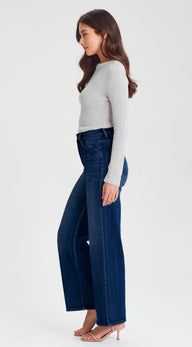 Woman wearing a white long-sleeve top and dark blue jeans on a white background