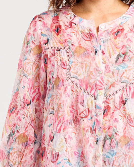 A close-up of a lightweight long-sleeve blouse with a pink, red, and blue floral print, featuring decorative embroidered details on the chest and a split neckline.