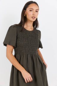 Woman wearing a green dress with smocked bodice on a white background
