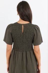 Woman wearing an olive green dress with smocked bodice on a white background