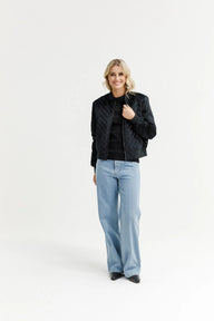 Woman wearing a black quilted jacket, black shirt, and light blue jeans on a white background