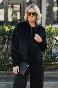 Woman wearing a black quilted jacket and sunglasses outdoors.