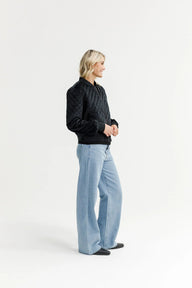 Person wearing a black quilted jacket and light blue jeans on a white background