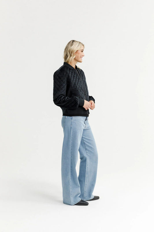 Person wearing a black quilted jacket and light blue jeans on a white background