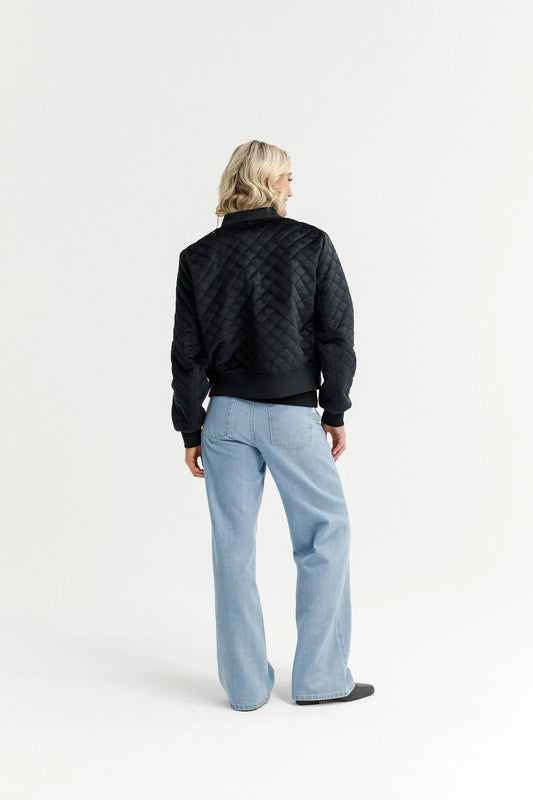 Person wearing a black quilted jacket and light blue pants on a white background