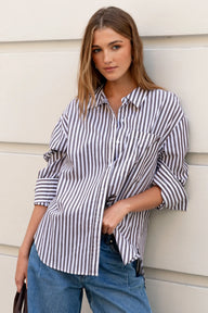 Woman wearing a striped shirt and blue jeans against a light-colored wall.