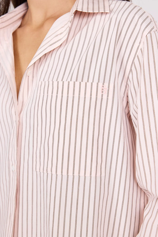 Close-up of a person wearing a light pink button-up shirt with thin vertical dark stripes and a chest pocket.