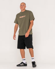 Man wearing an olive green t-shirt with 'Rusty' logo and black shorts on a white background