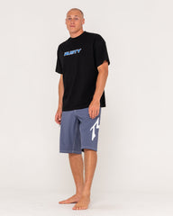 Man wearing a black t-shirt with 'Rusty' logo and gray shorts on a white background