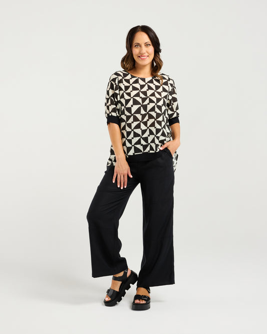 Woman wearing the Zafina Havana top with geometric pattern and black pants on a white background