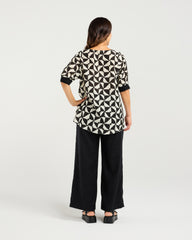 Woman wearing the Zafina Havana top with geometric pattern and black pants on a white background