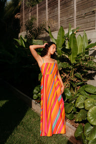 Woman in a colorful dress standing in a garden with large green leaves.
