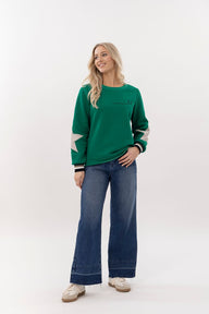 Woman wearing a green sweater with white sleeves and blue jeans on a white background