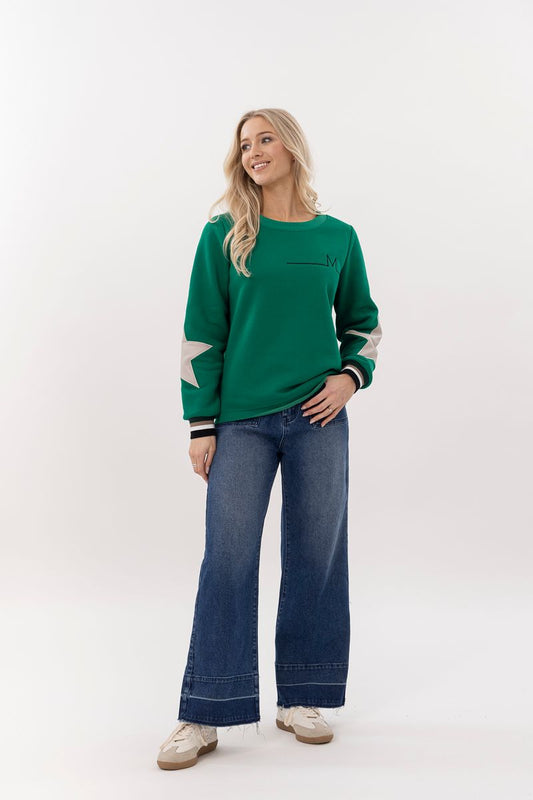 Woman wearing a green sweater with white sleeves and blue jeans on a white background